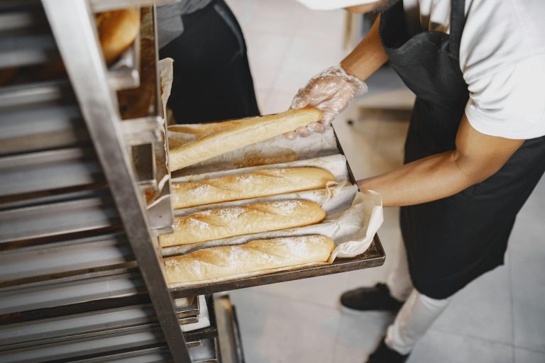 A baker arranges freshly baked baguettes on a rack, wearing gloves for hygiene.