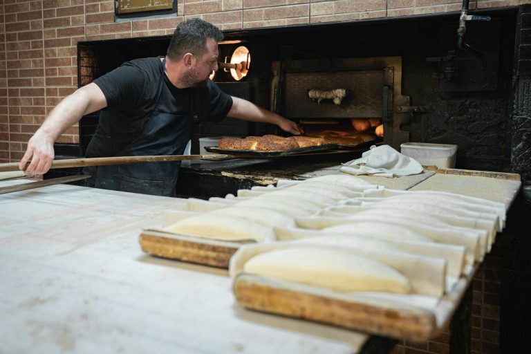 A baker uses a traditional wood-fired oven to bake fresh bread, showcasing artisan baking skills.